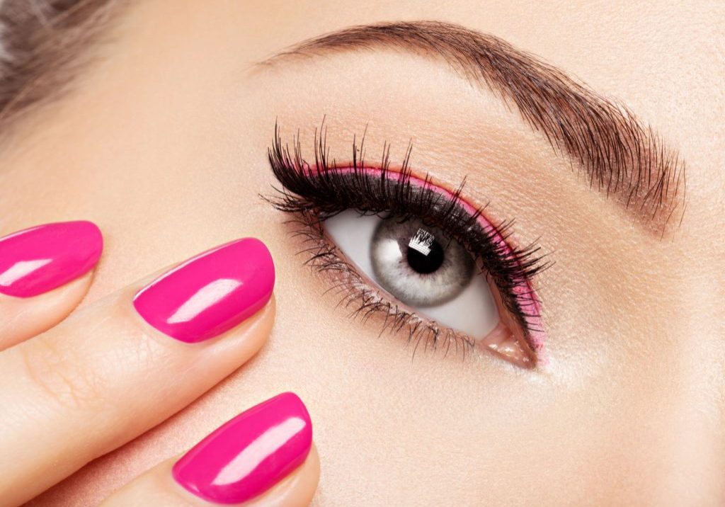 Closeup woman face with pink nails near eyes. Fingernails with pink manicure